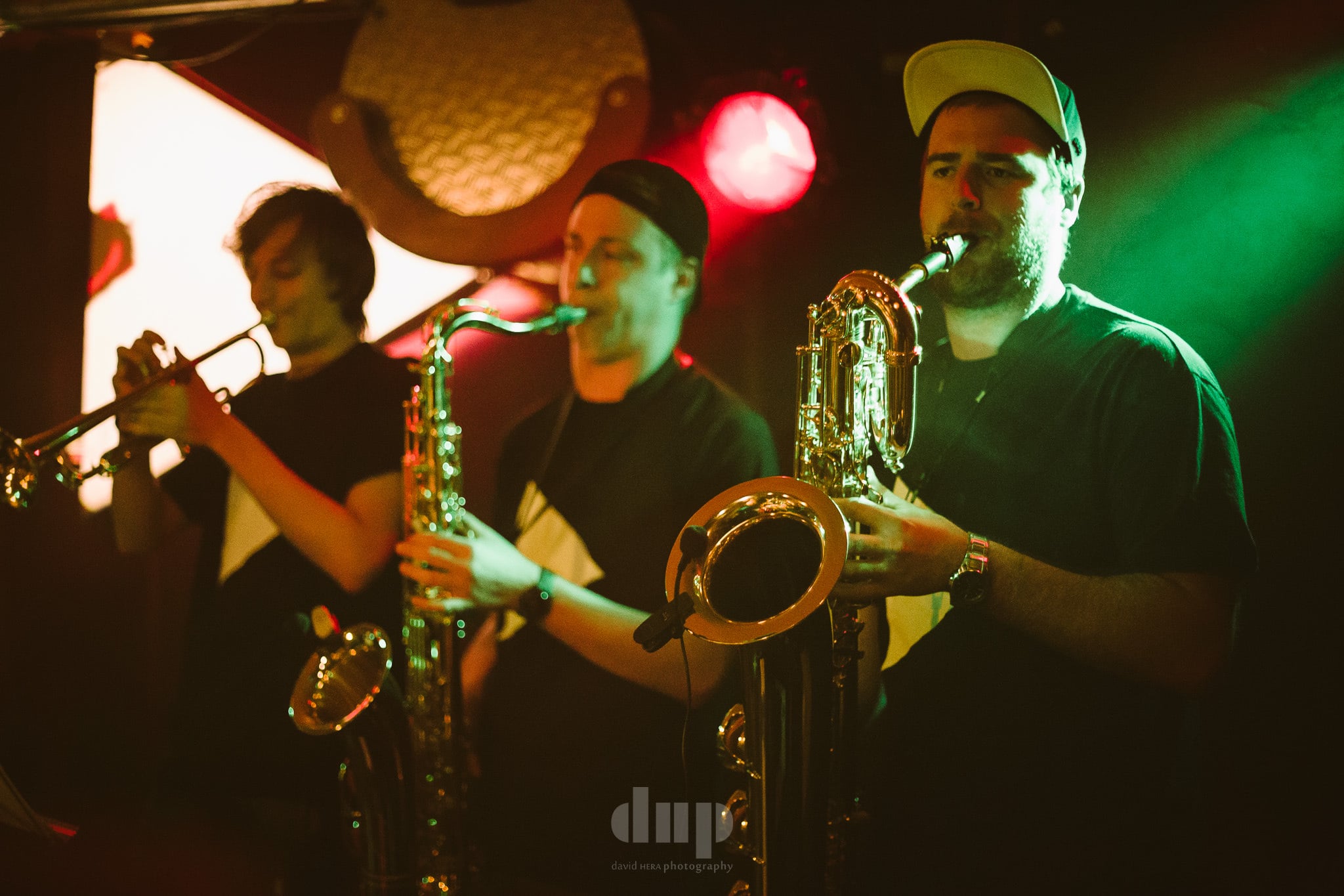 Horn section playing under red and green stage light.