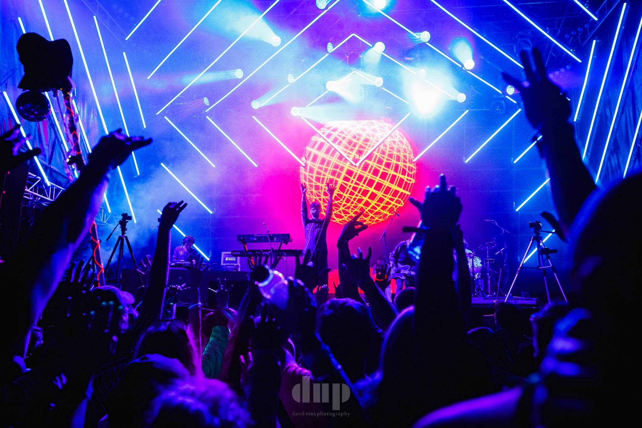 Crowd with hands raised under laser lights at a festival stage.