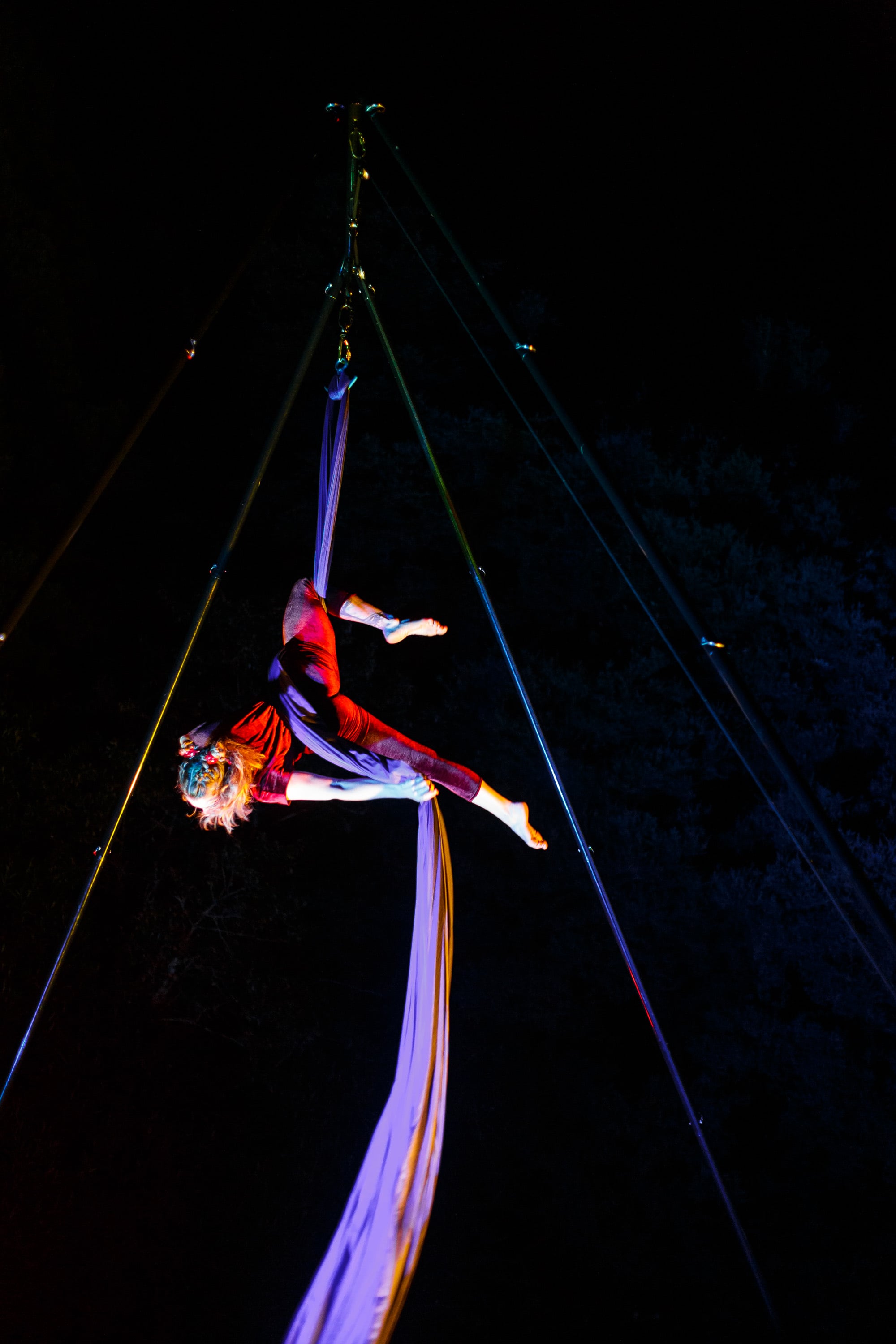 Aerial silks performer high above a dark stage.