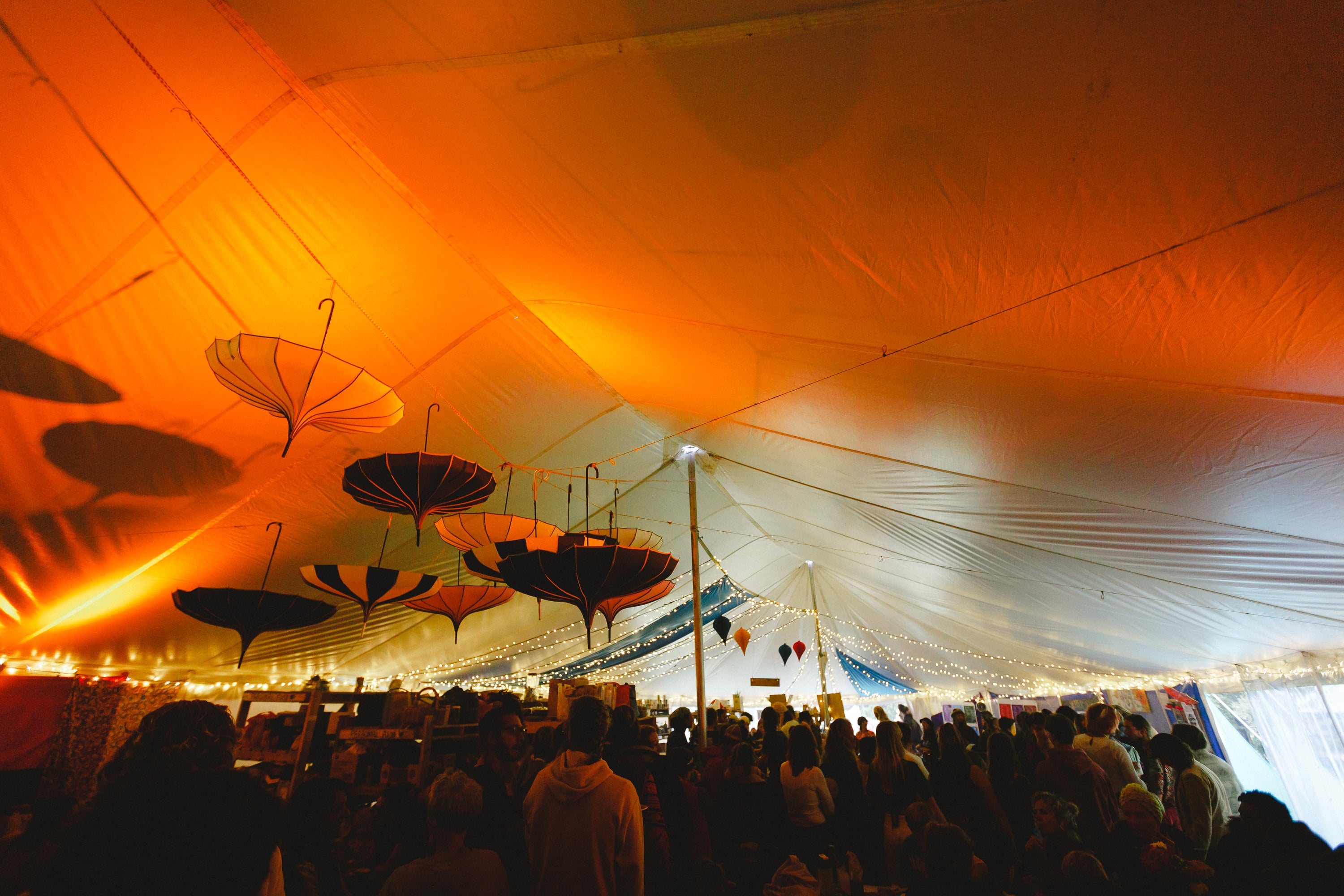 Festival crowd under an orange-lit big top hung with umbrellas.
