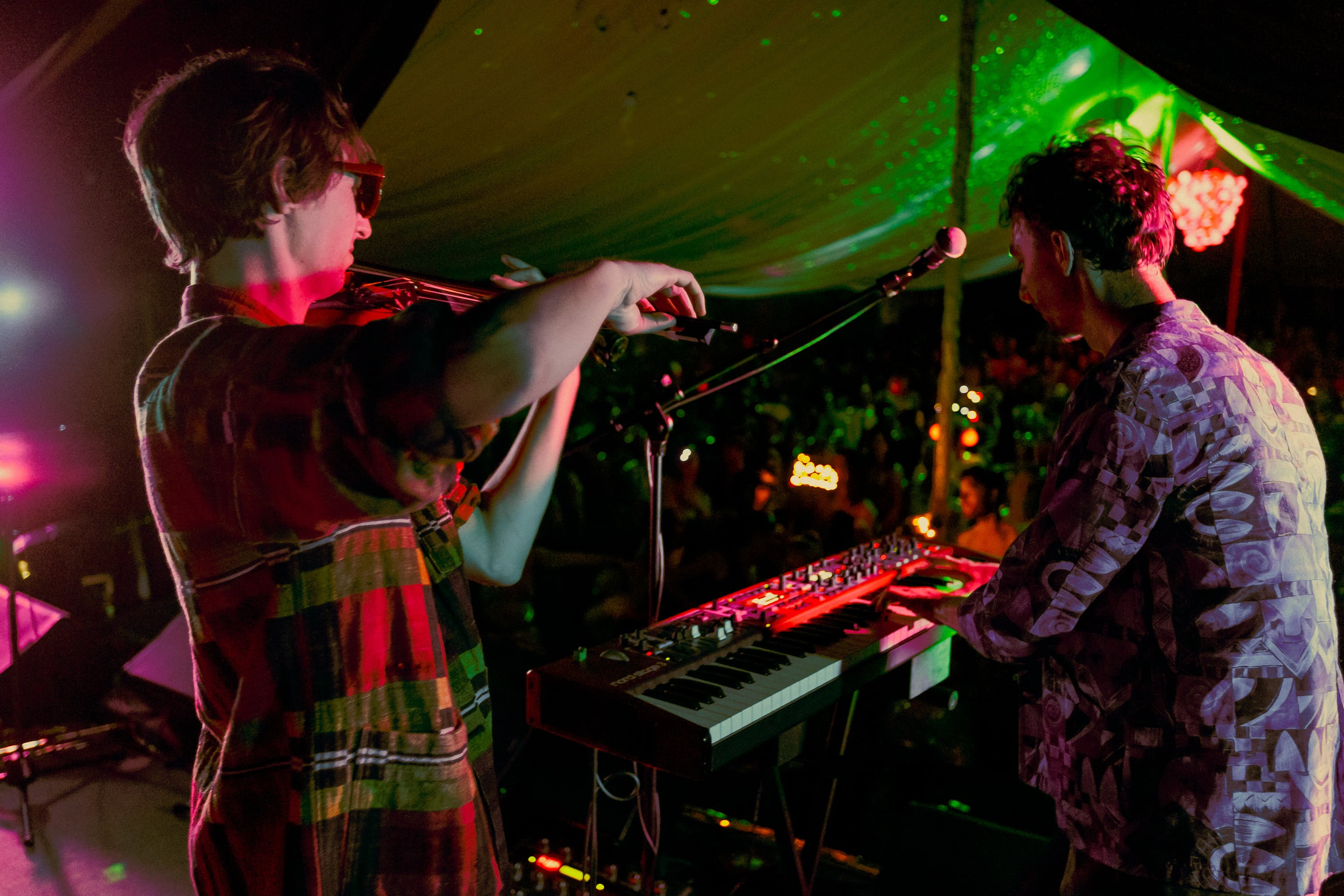 Violinist and keyboardist playing under coloured lights.