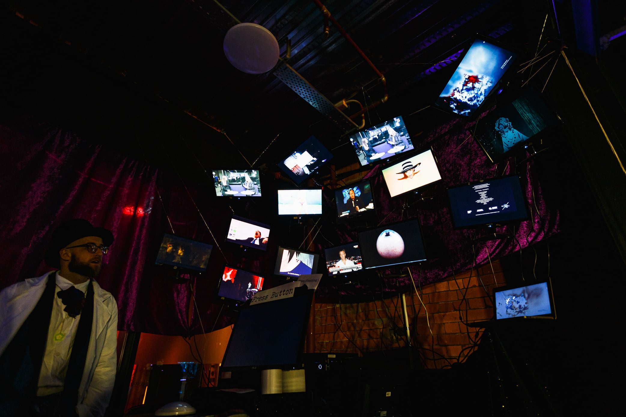 Costumed guest beneath a wall of hanging screens.