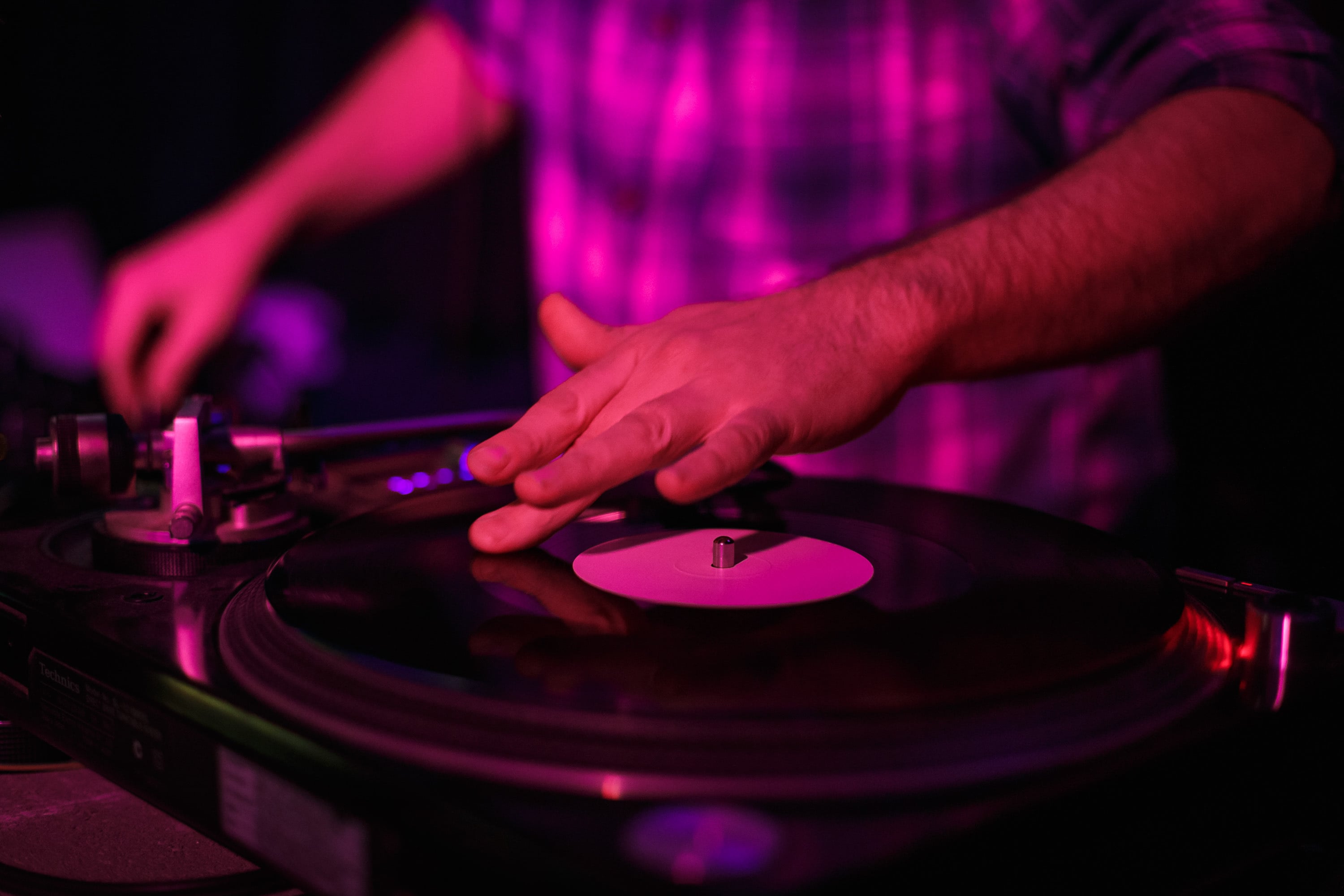 DJ’s hand on a spinning record under pink light.