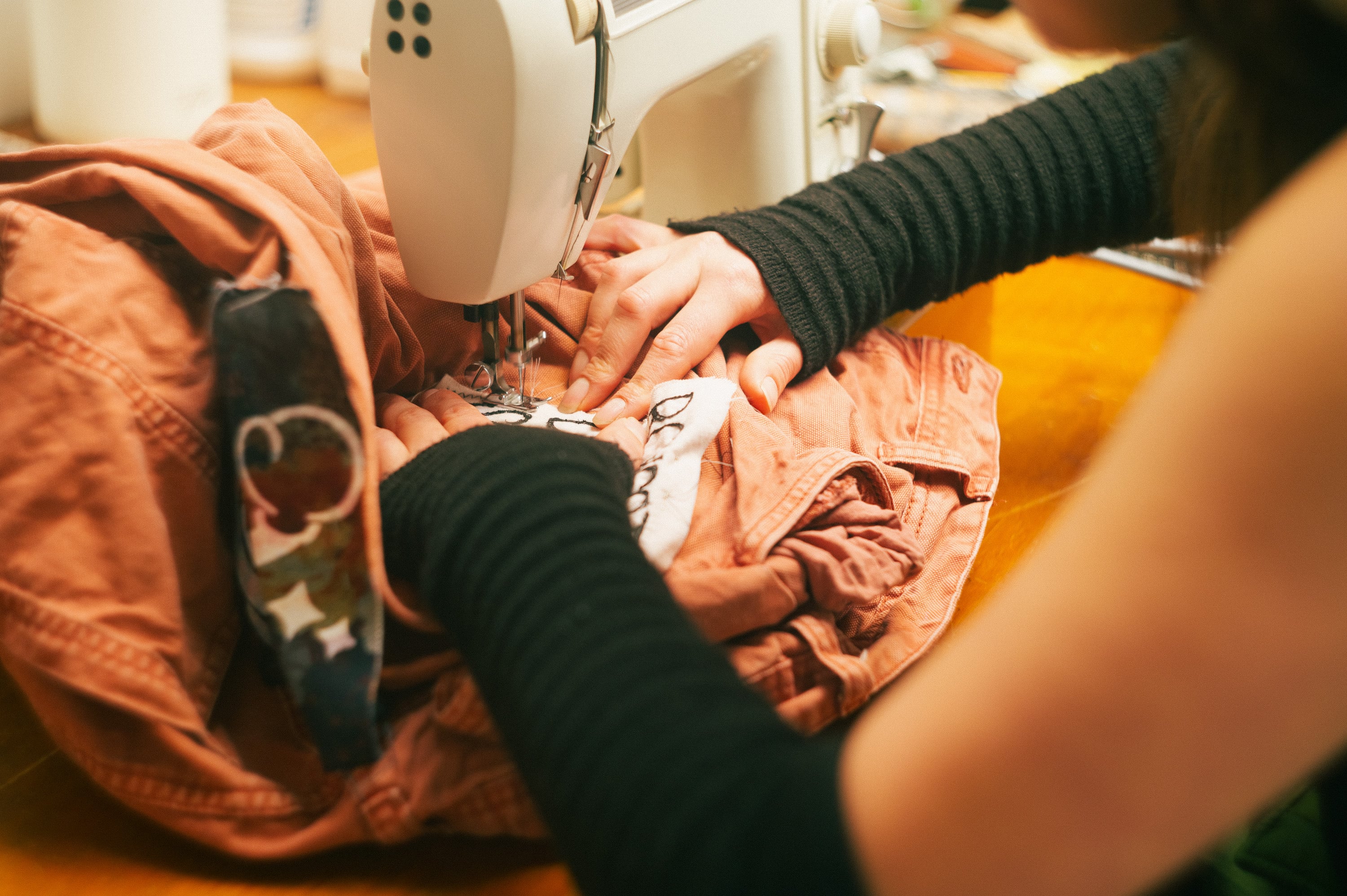 Hands guiding fabric through a sewing machine at a repair stall.