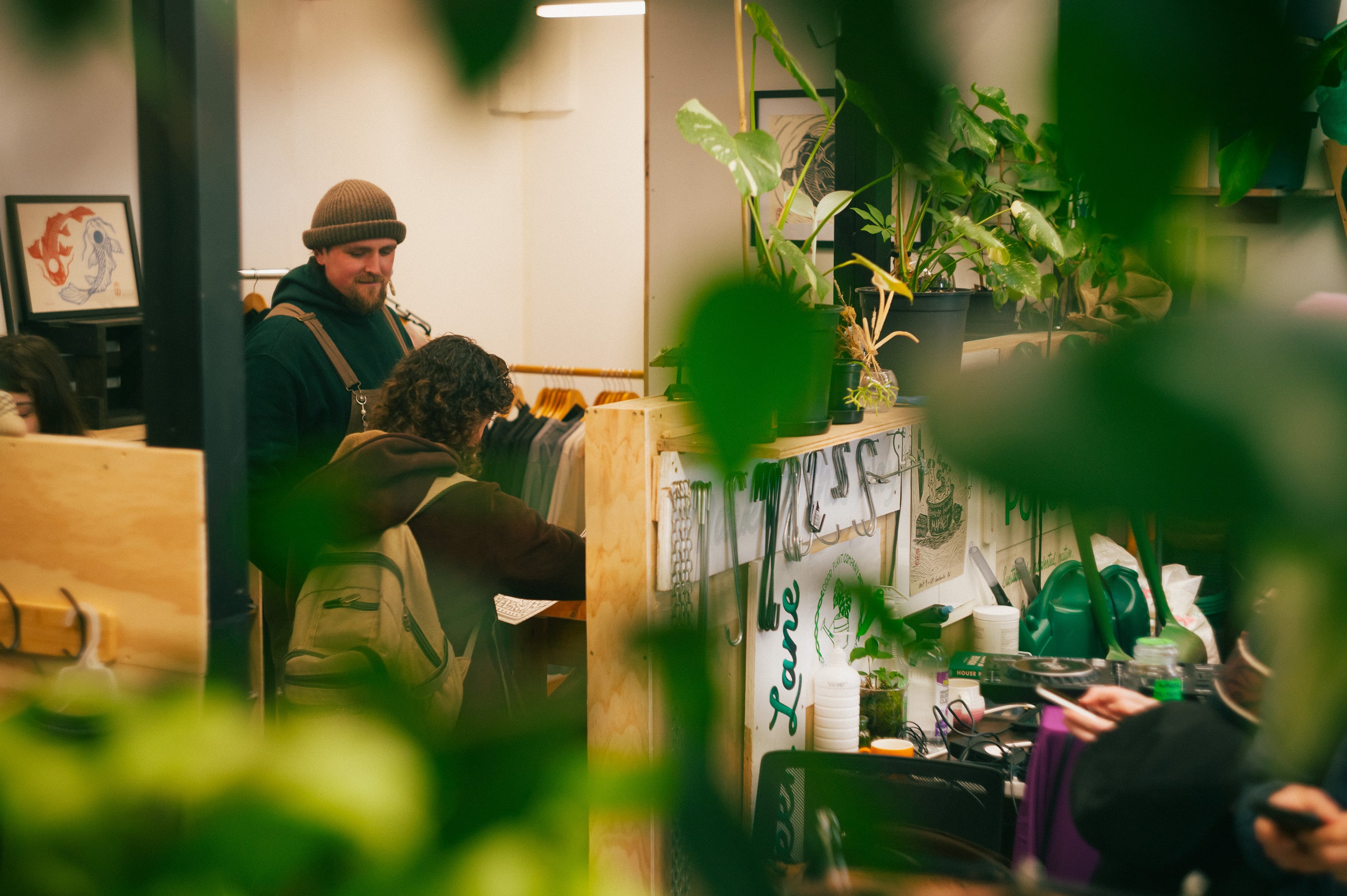Shoppers browsing a market interior framed by houseplants.