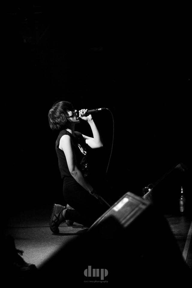 Singer crouched at the front of a dark stage, black and white.