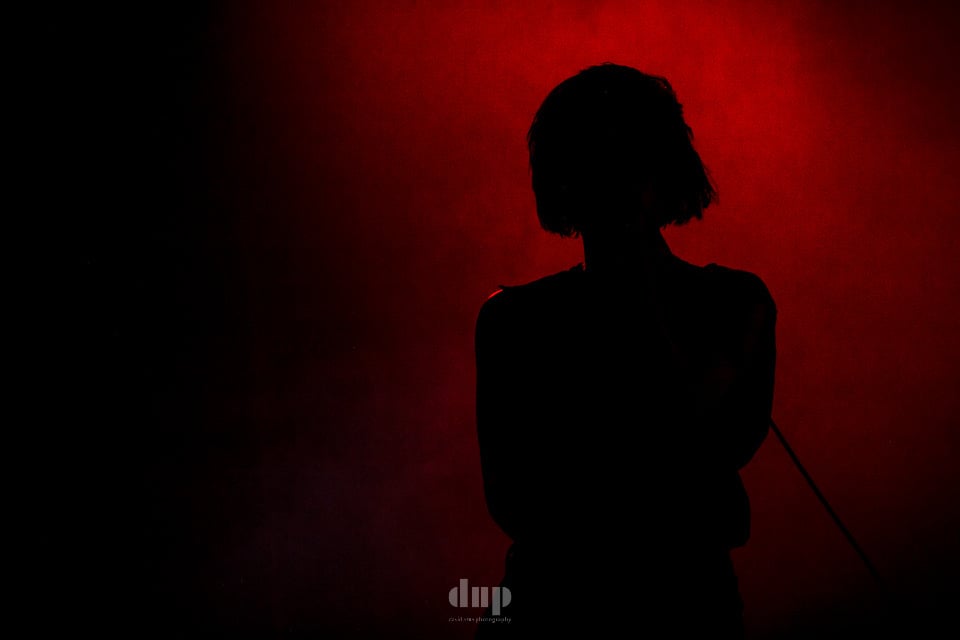 Silhouetted singer against a deep red backdrop.
