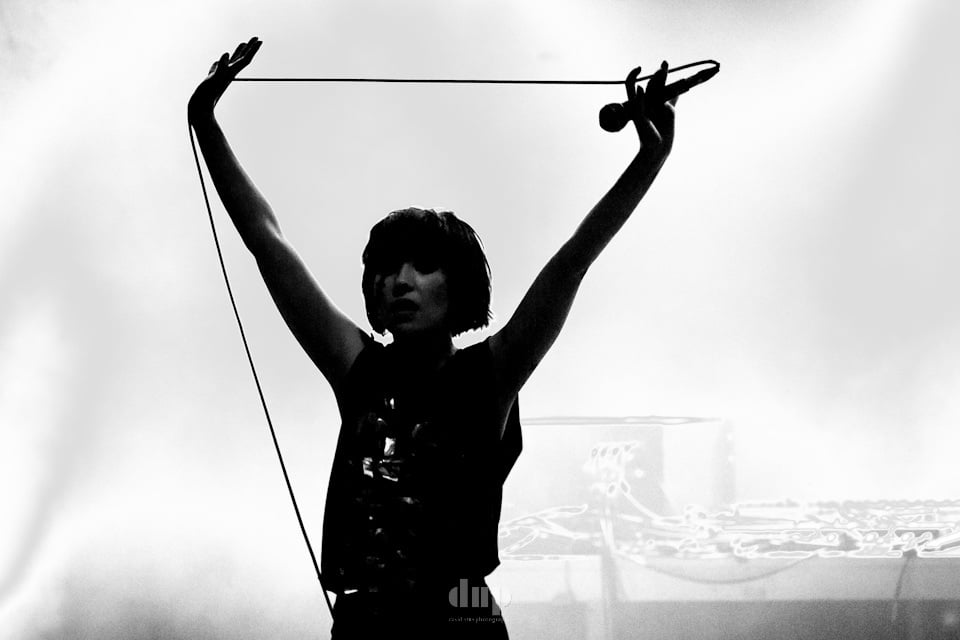 Singer with arms raised, mic cable arcing overhead, black and white.
