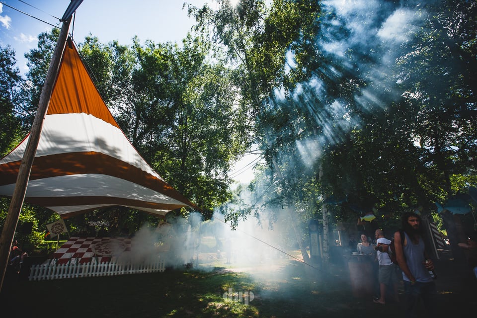 Sunlight through trees over a striped festival tent.