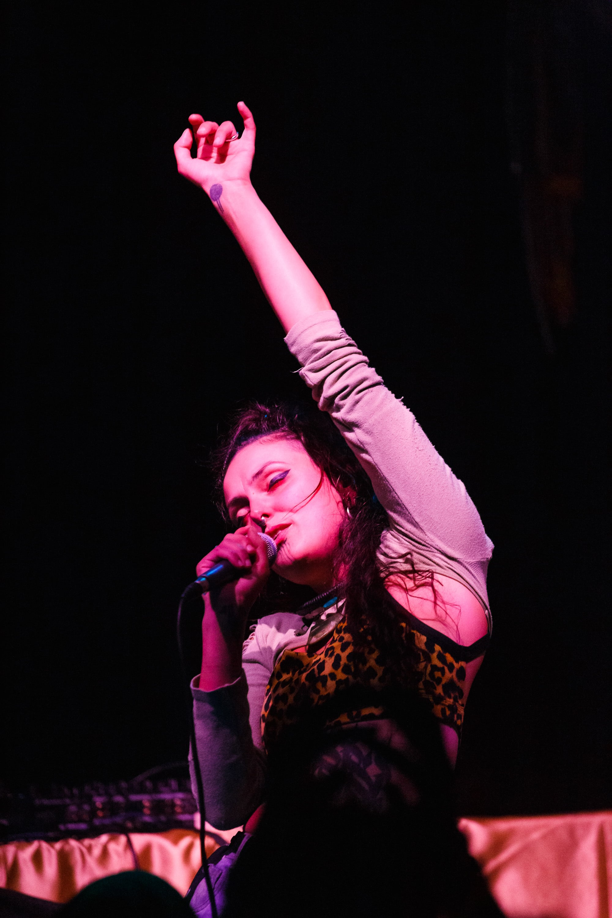 Singer with arm raised under magenta light.