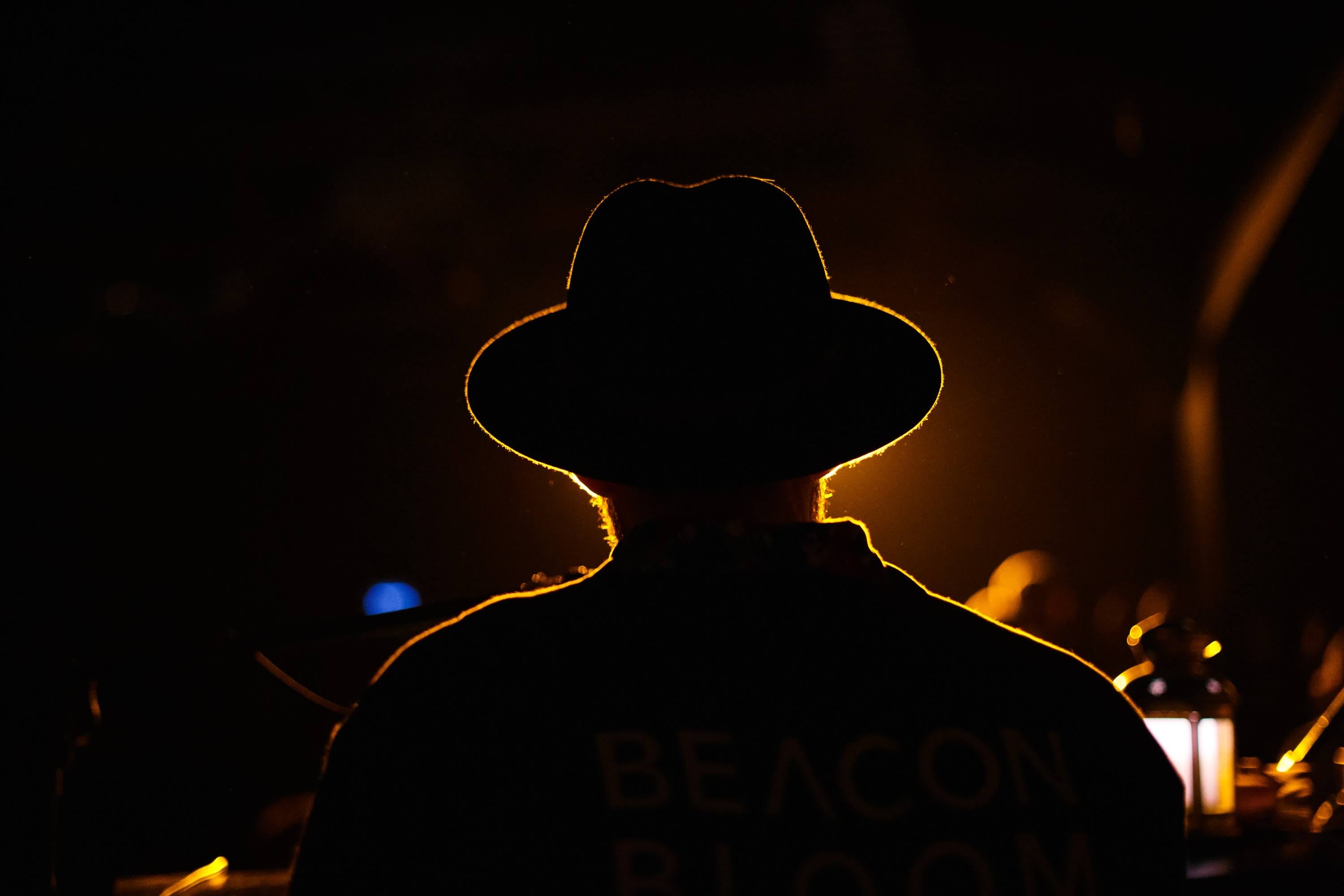 Musician in a wide-brimmed hat, rim-lit in gold from behind.