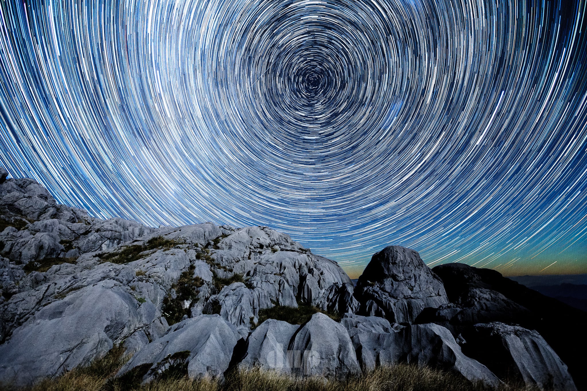 Star trails circling above limestone boulders.