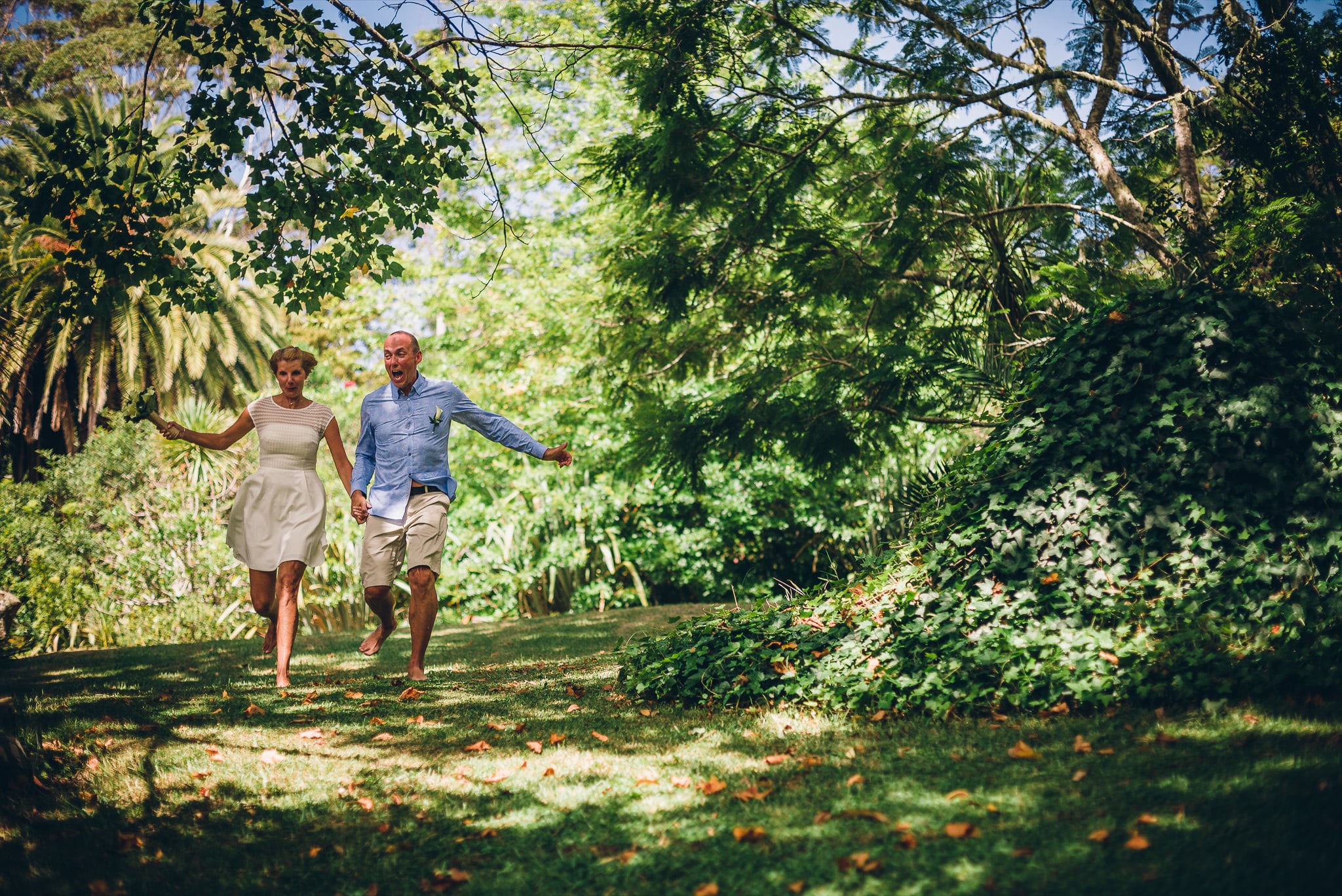 Couple running hand in hand through a garden.