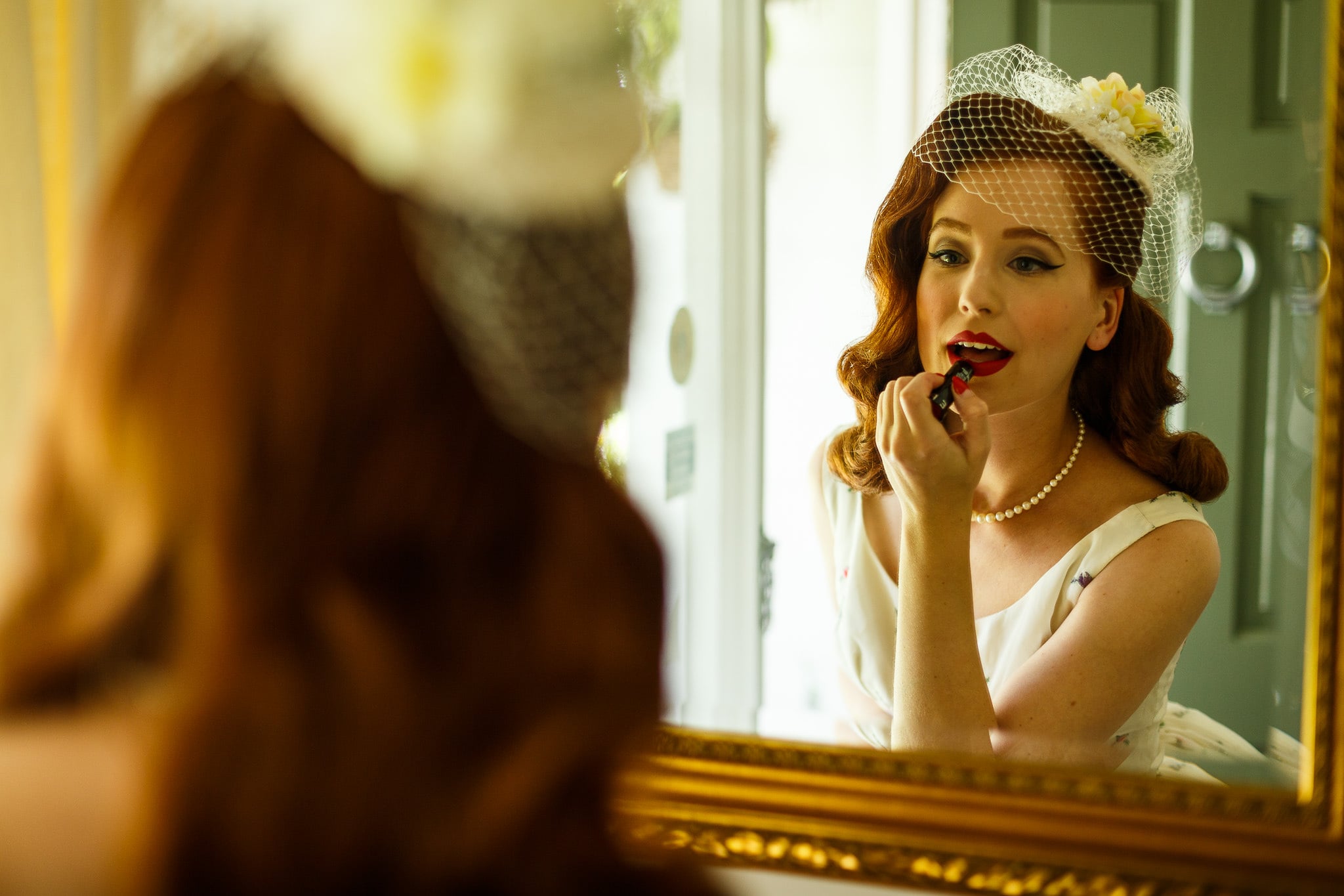 Bride applying red lipstick in a gilded mirror.