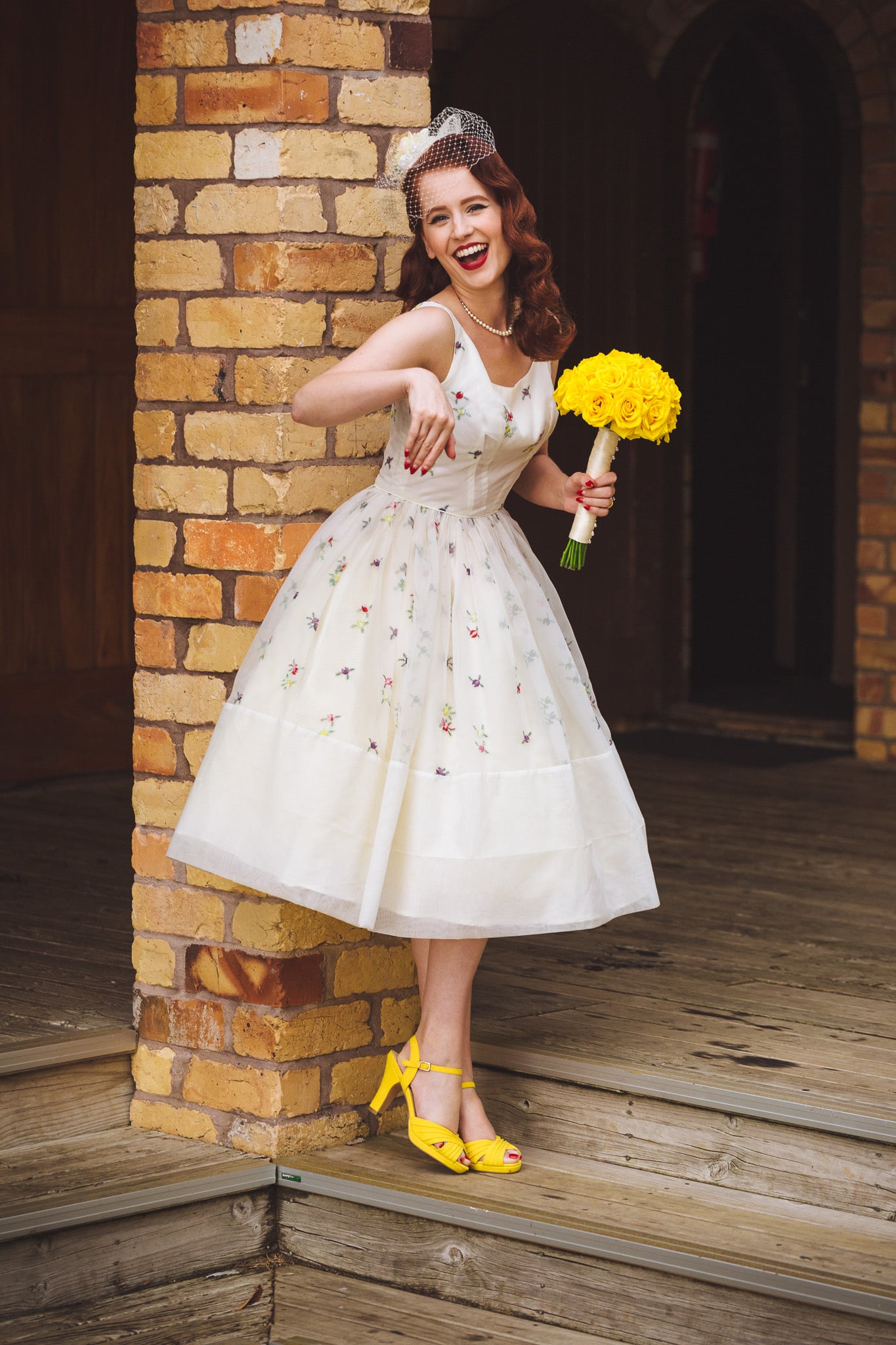 Bride laughing in a doorway, holding yellow flowers.