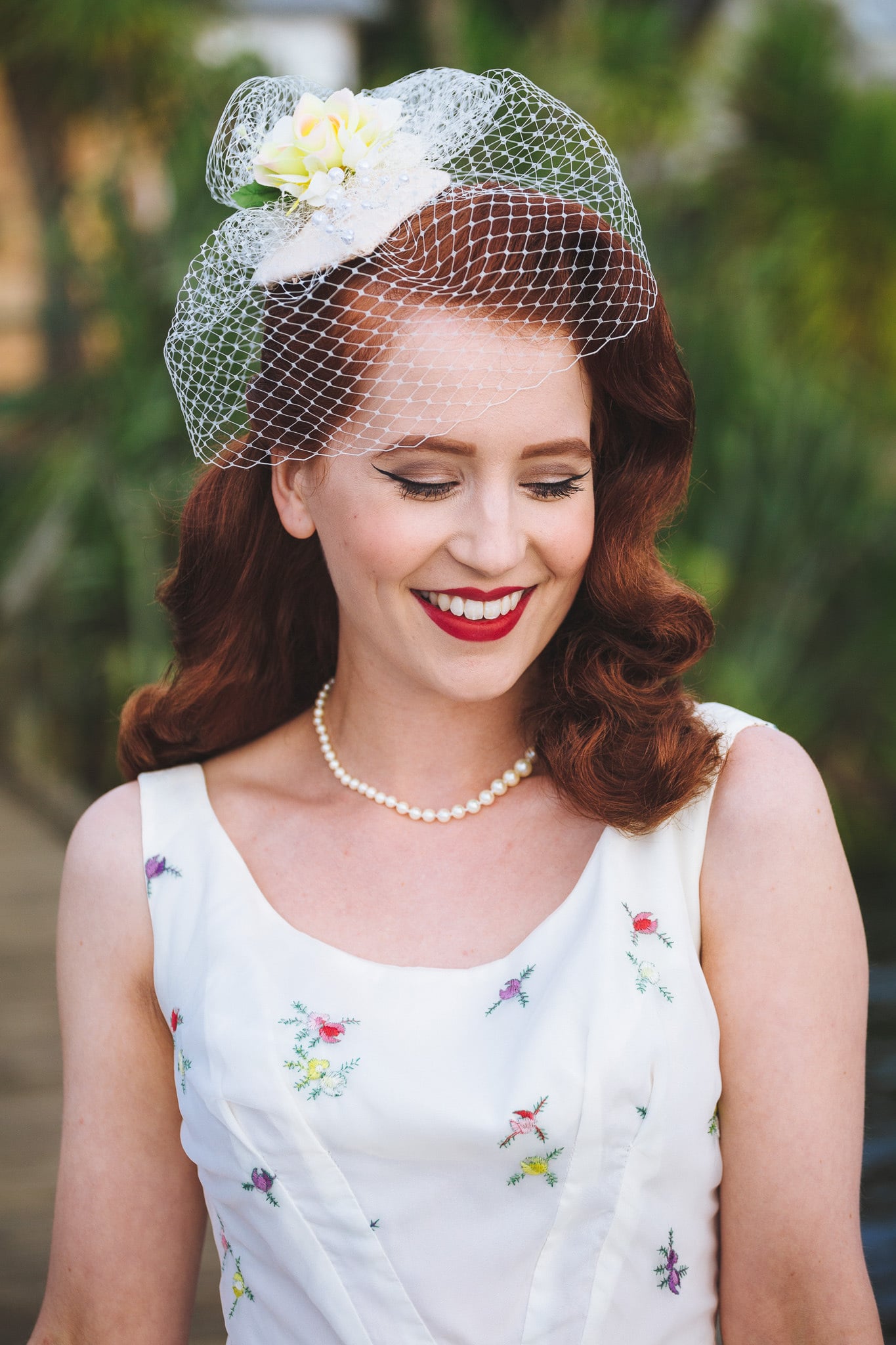 Bride in a vintage birdcage veil, looking down with a smile.