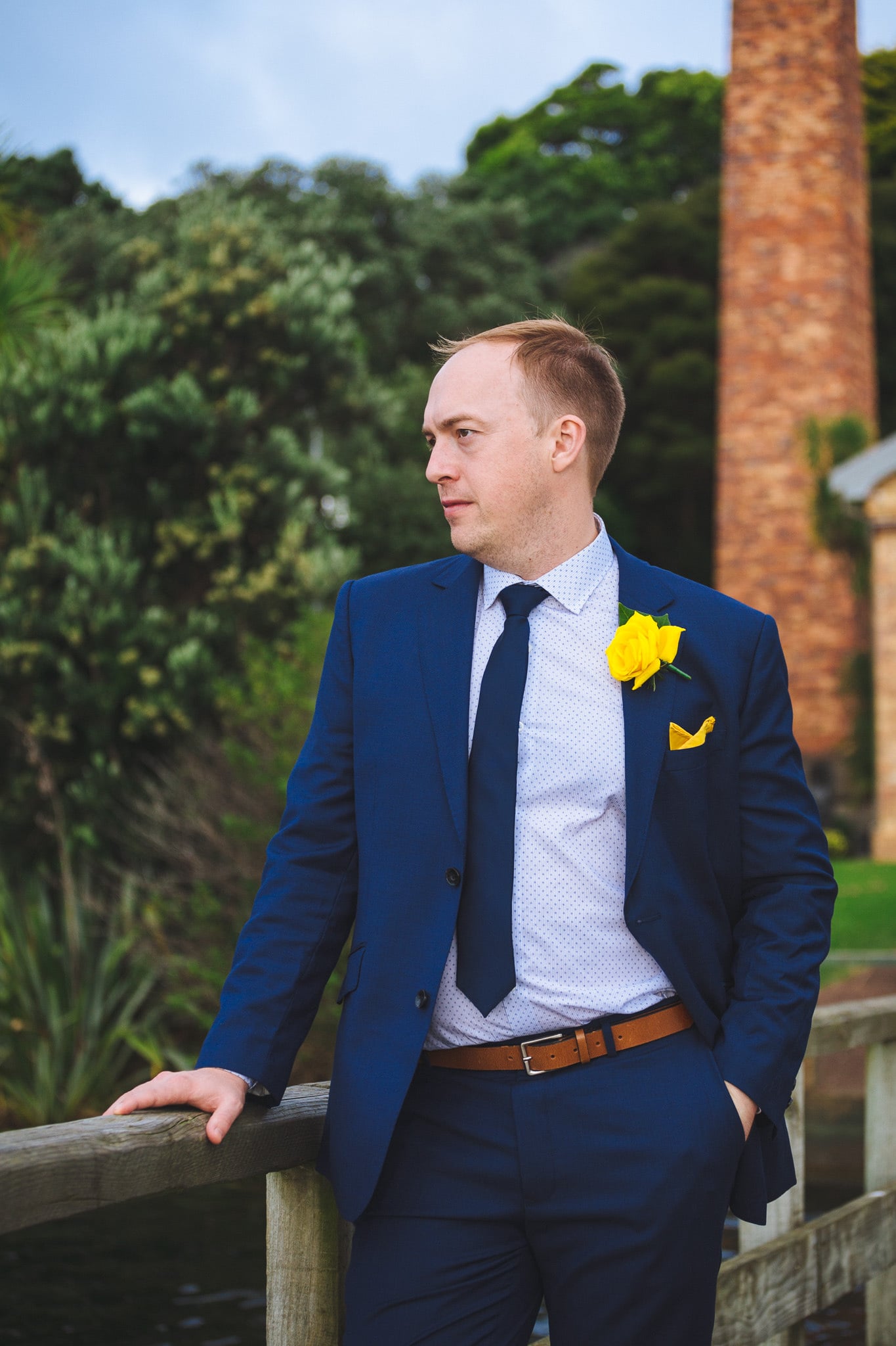 Groom in a navy suit with a yellow rose, by the water.