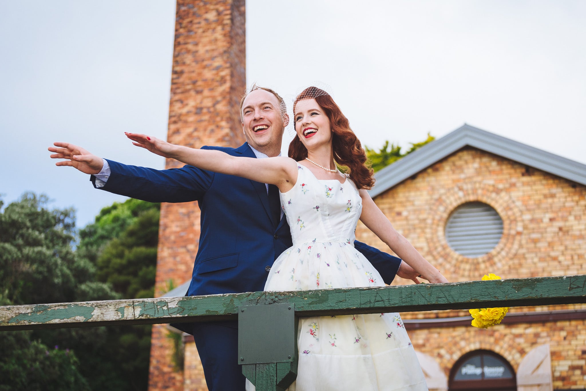 Couple with arms outstretched beside a brick chimney.