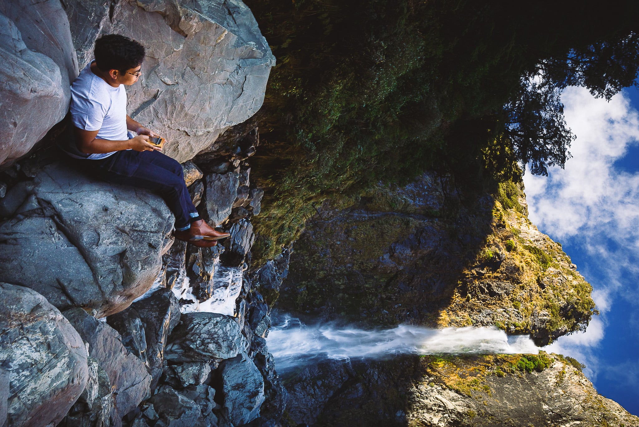 Boy sitting on rocks beside a waterfall.