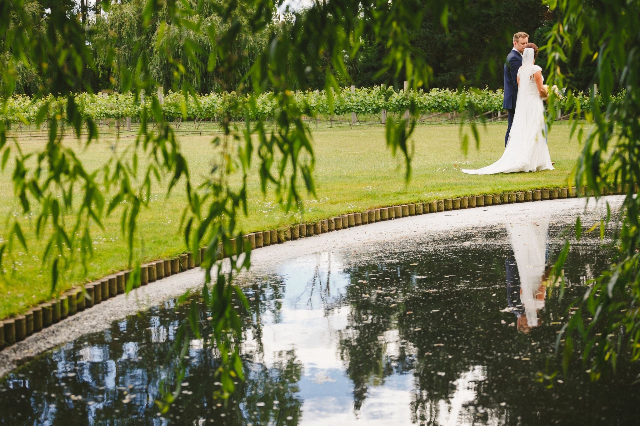 Couple reflected in a pond under willow trees.