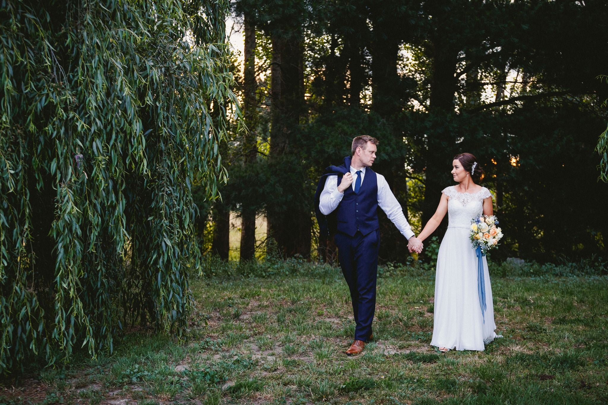 Couple walking hand in hand between willows.