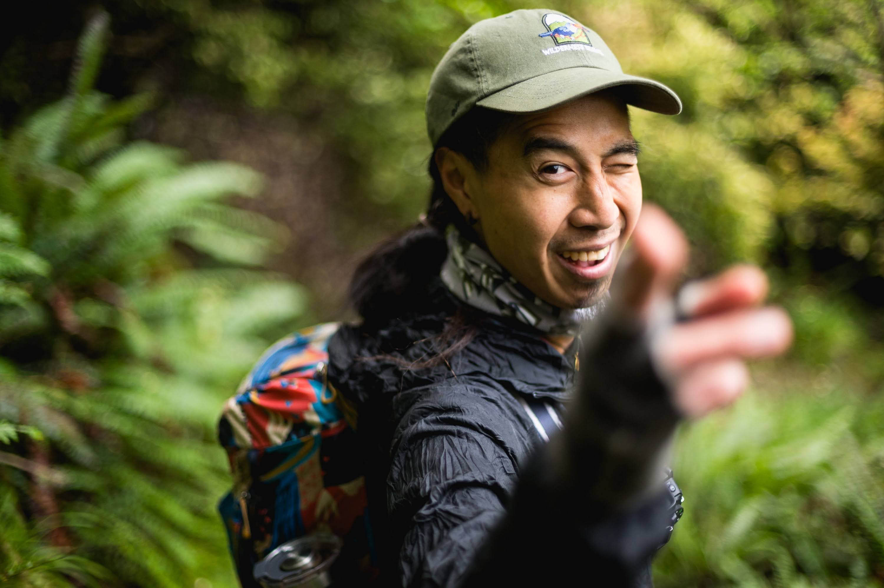 Laughing hiker in a cap reaching towards the camera in the bush.