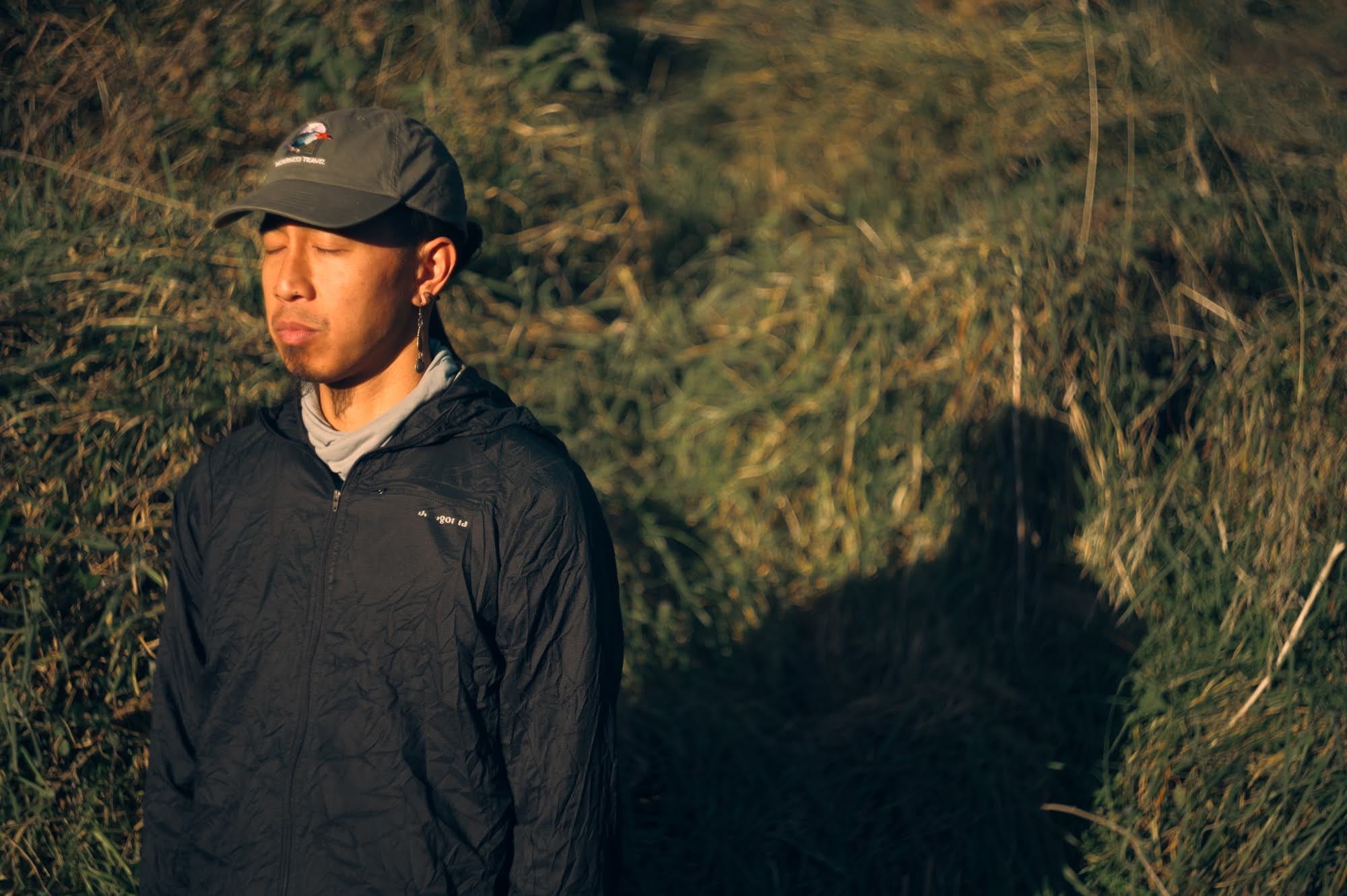 Man in a cap with eyes closed in low golden light.