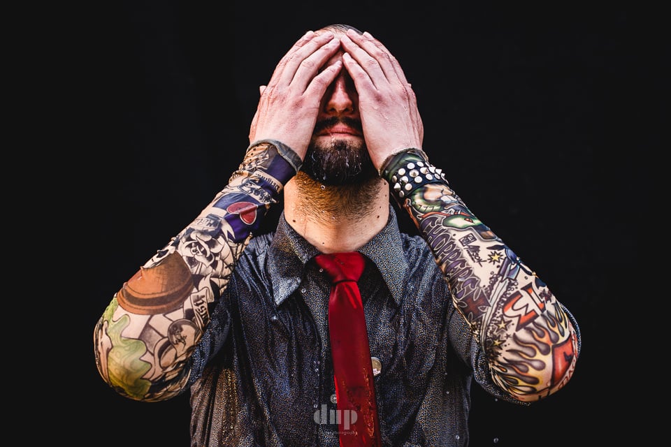 Tattooed performer with hands covering their face.