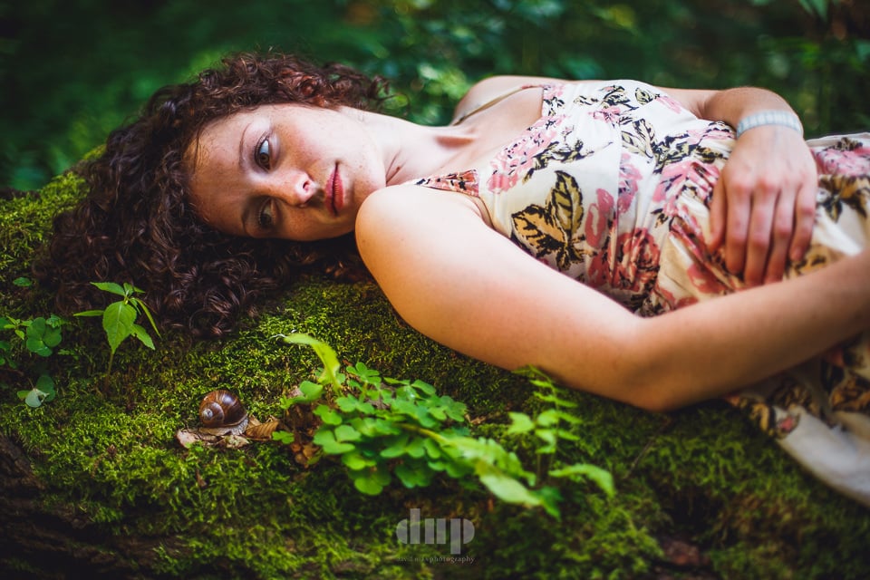 Woman with curly hair lying on a mossy forest floor.