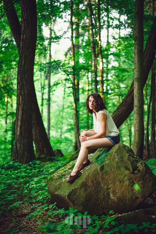 Woman sitting on a mossy boulder in a green forest.