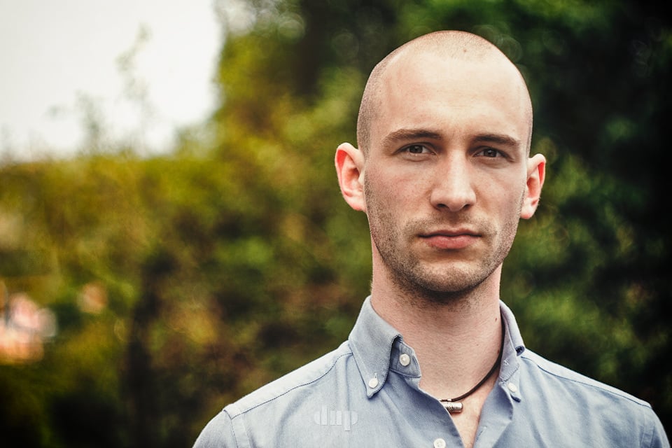 Man in a linen shirt in front of a hedge.