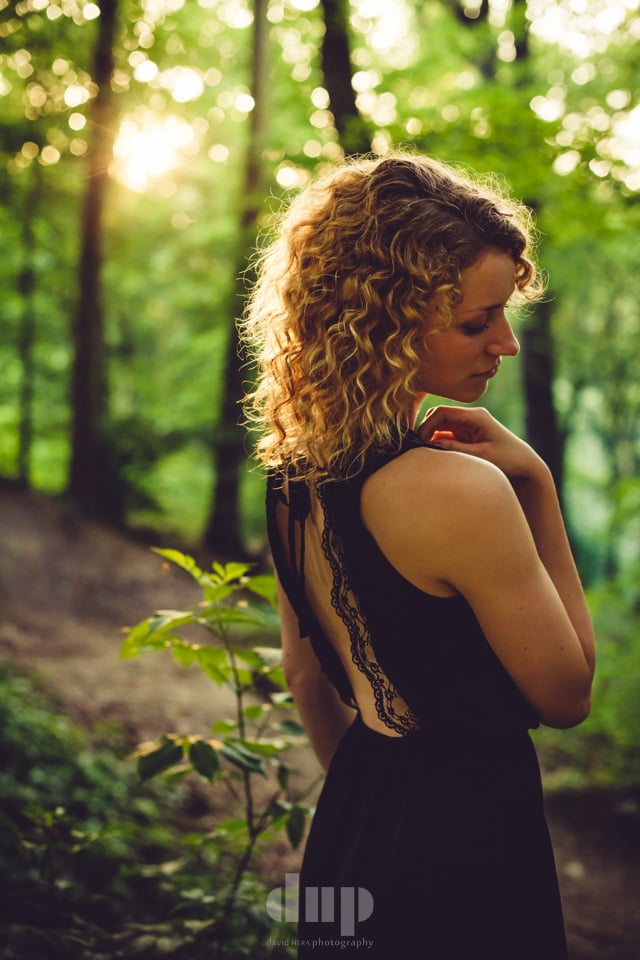 Woman in a backless dress in a sunlit forest.