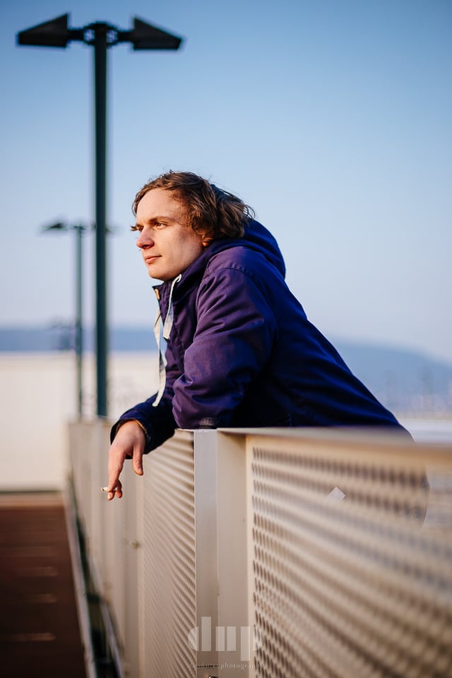 Musician leaning on a bridge railing by the river.