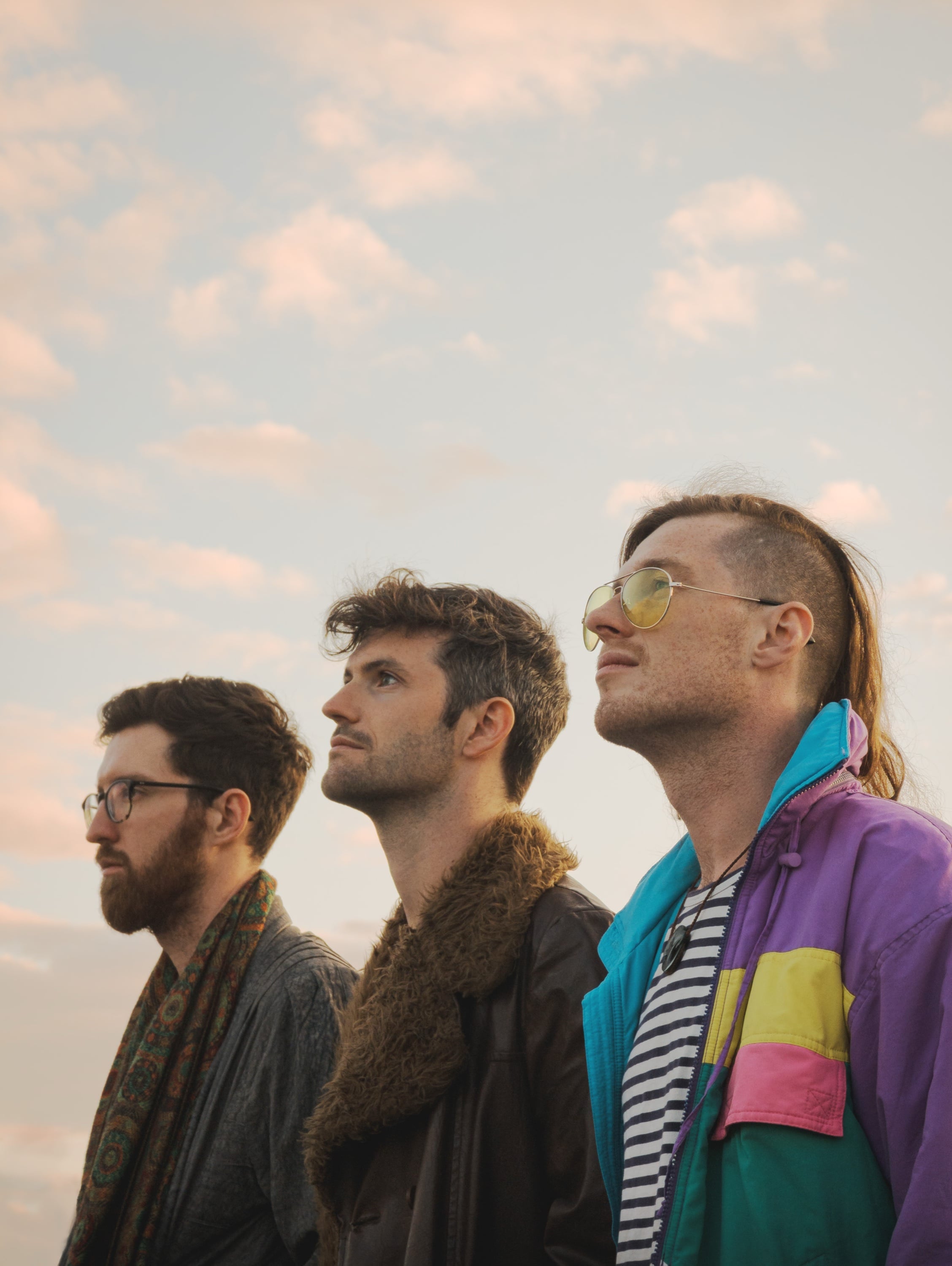 Three-piece band posing against a soft evening sky.