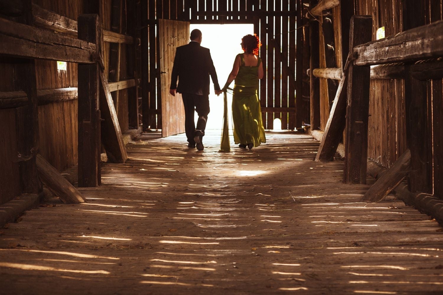 Couple walking out of a timber barn into the light.