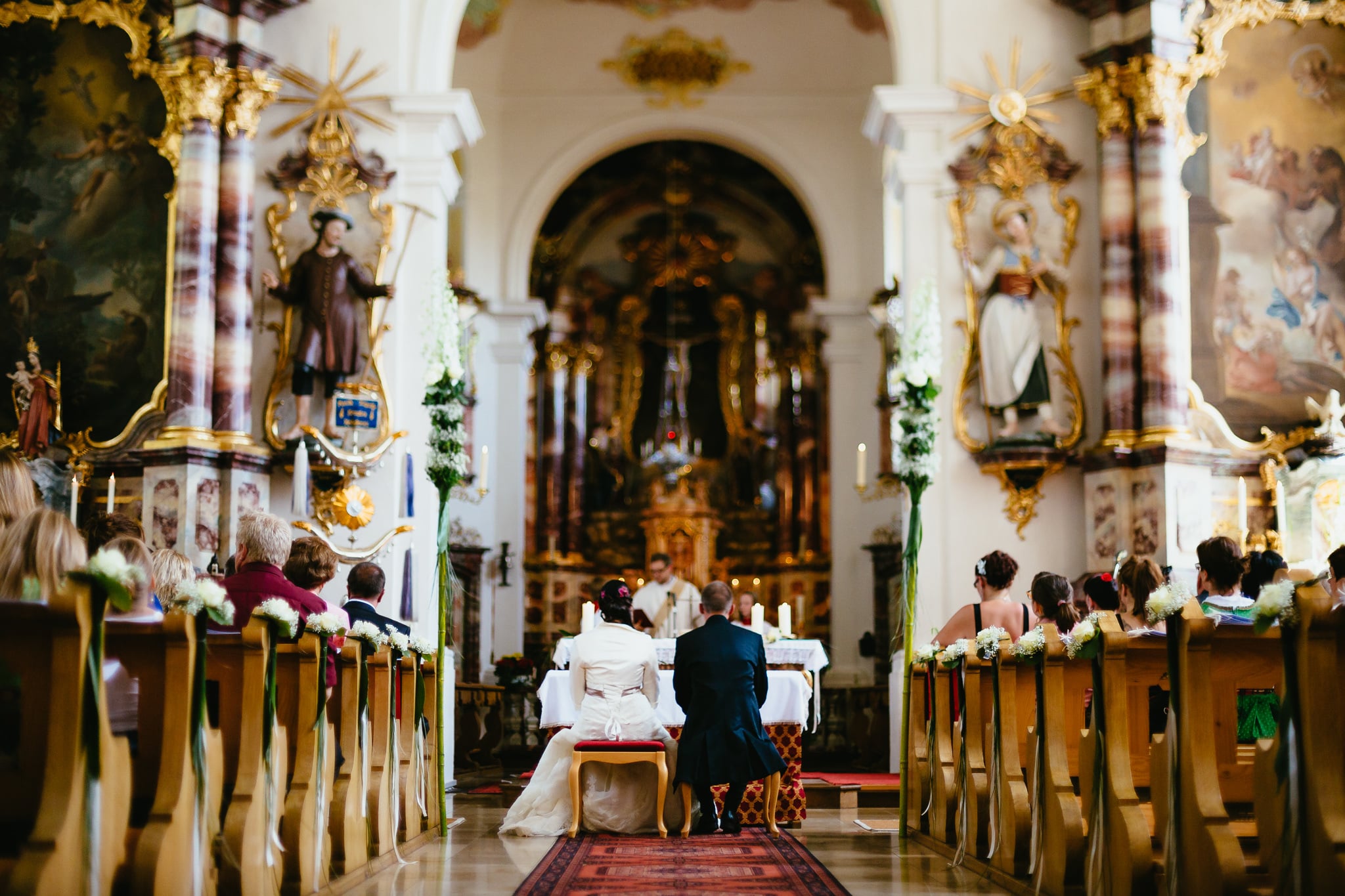 Church wedding ceremony beneath a baroque altar.